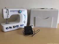 Full view of the Shark Euro-Pro X sewing machine, black foot pedal, and white carrying case on a wooden surface.