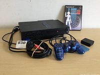 Photo showing Sony PlayStation 2 console with cables, translucent blue DualShock 2 controller, memory card, power adapter, and Persona 3 FES game case.