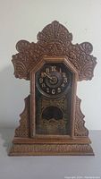 Front view of the antique mantel clock showing carved wood details and clock face with gold numerals.