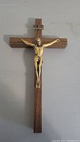 Full view of crucifix against wall showing wooden cross and brass Jesus figure with INRI plaque.