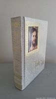 Front cover of Bible, white textured hard cover with gold embossing and framed image of Jesus Christ.
