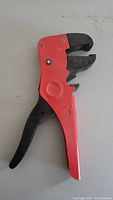 Full view of the self adjusting wire stripper with red handle and black trigger and jaws.