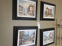 Four framed cityscape paintings arranged on a wall, showing varying street views with pedestrians and buildings