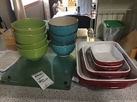 View of the ceramic bowls stacked in green and blue colors beside three glass cutting boards and red/white baking dishes.
