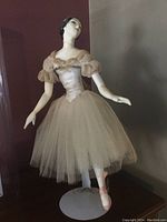 Front view of vintage porcelain ballerina figurine in beige tulle skirt standing on metal stand.