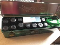 Opened metal green tin box displaying multiple small amber glass essential oil bottles with black caps, and a boxed set of Rose & Robin essential oils inside.