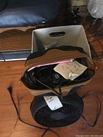 Photo showing a tan storage container holding hair clippers, Black and Decker iron, and Honeywell fan with power cord visible.