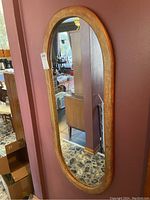 Full view of the oval wooden framed mirror hung on wall, showing size, shape, and overall condition.