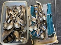 Two plastic bins filled with assorted sterling flatware and a folded cleaning cloth