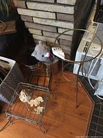 Four metal plant stands with different shapes and sizes, a silver cylindrical bucket with plush mouse inside, and elephant wind chimes on the floor near a brick fireplace.