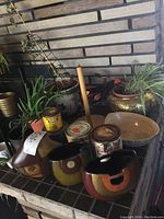 Photo showing three multi-colored ceramic vases with patchwork earth tone colors surrounded by small cans and plant pots with alive plants