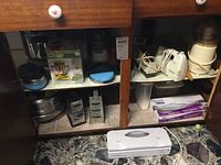 Wide view of wooden cabinet showing kitchen appliances and utensils including a white hand mixer, food processor, vegetable chopper, metal grater, and small kitchen accessories.