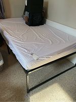 Full view of single bed frame with mattress and items on top, showing fitted sheet over mattress and black metal frame with simple design.