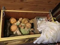 Four vintage Cabbage Patch Kids dolls inside a wooden chest, showing details of their soft bodies and pastel-colored outfits.