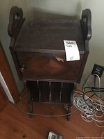 Full view of vintage small wooden table showing top, door with veneer damage, side handles, and lower slots.