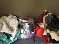 Lot of womans clothing including jackets, coats, tops, bottoms displayed on a couch with hangers and bags