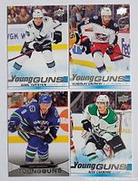 Four Young Guns rookie hockey cards laid out, featuring Danil Yurtaykin, Vladislav Gavrikov, Gordie Howe, and Nick Aamano in team jerseys. Player action shots on ice rink backgrounds.