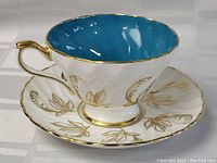 Close-up of Aynsley porcelain tea cup showing blue interior, white exterior and gold floral patterns