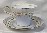 Tea cup with floral and gold detailing on white china placed inside matching saucer.