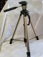 Camera tripod with silver metal legs and black plastic parts, handle extended, standing on white background.
