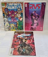 Three comic books positioned standing: The Infinity Gauntlet, RV9 #1, and X-Force War Realms issue.