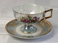 Photo showing side view of the tea cup on the saucer, highlighting the floral pattern and gold handle.