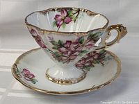 Tea cup and saucer showing scalloped edges, floral paint, and gold trim