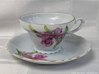 Side view of porcelain tea cup showing pink floral pattern, gold rim, and scalloped edges