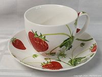 Side view of the tea cup on the saucer showing the strawberry and leaf design.