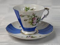 Porcelain tea cup and saucer set shown from side view highlighting blue and floral rose designs with gold trim