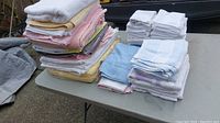 Stacked assorted bath towels and smaller towels laid on a table outdoors, showing various colors and sizes