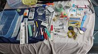 Wide view of the assorted sewing accessories laid out on a cloth including measuring tools, scissors, pins, threads, and small sewing tools.