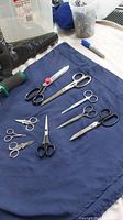 Eight sewing scissors arranged on a dark blue cloth showing varied styles and sizes.