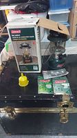 Green Coleman gas lantern with original box and accessories on black surface