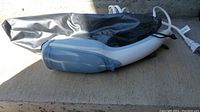 Conair handheld garment steamer lying on a concrete surface with fabric travel bag behind it.