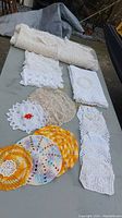 Photo showing a range of crocheted and knitted doilies in white, beige, yellow, orange, and multicolored yarns with different patterns laid out on a surface.