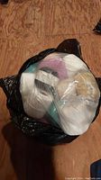 Top view of several crochet thread spools packed inside a black plastic bag, showing colors including white, beige, and pastel shades.