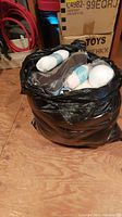 Black garbage bag filled with various colored skeins and balls of wool yarn, including white and pink.