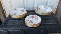 Photo of stacks of dinner plates, smaller plates, and bowls with floral pink rose designs and gold trim.