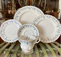 Five-piece Royal Albert Memory Lane china set displayed showing teacup, saucer, bread plate, salad plate, and dinner plate with blue forget-me-not floral pattern.