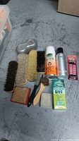 Full view of shoe brushes, sprays, leather dye, polish tube all laid out on gray surface