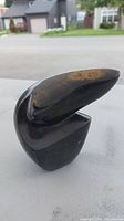 Side view of black stone carving showing smooth polished surface and abstract intersecting shapes.