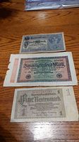 Three German banknotes laid flat on a wood surface showing 5 Mark 1917, 20,000 Mark 1923, and 1 Mark 1937 notes.
