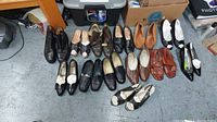Photo showing full lot of various women's shoes on gray floor including flats, heels, sandals in multiple colors.