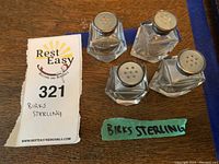 Four Birks sterling salt and pepper shakers on wooden surface with label showing lot number and 'Birks Sterling' written on tape.