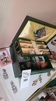 Green velvet-lined jewelry box with compartments holding costume brooches and earrings, some rhinestone decorated. Jewelry box lid has a mirror. Items displayed inside box and on the surface around it.
