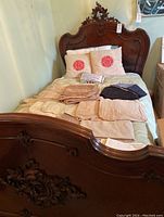 Full view of carved bed frame with assorted linens laid out