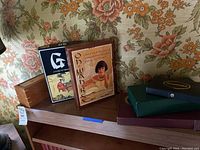 Photo of boxed Go and Oh Wah Ree games and a red game box on top of a wooden shelf with floral wallpaper background.