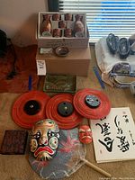 Photo showing entire lot setup with sake set, plates, lanterns, masks and accessories on floor with window in background