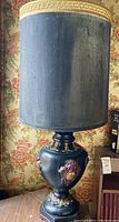 Full view of one table lamp with navy blue cylindrical fabric shade and ornate urn base with embossed gilded details.